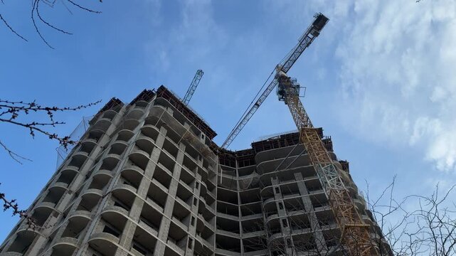 A towering crane works on a large concrete high-rise against a bright, cloudy sky. The sight feels impressive and symbolizes the steady heartbeat of city life.