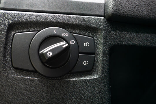 Close up of a modern car headlight control switch dial and fog light buttons on a black textured dashboard