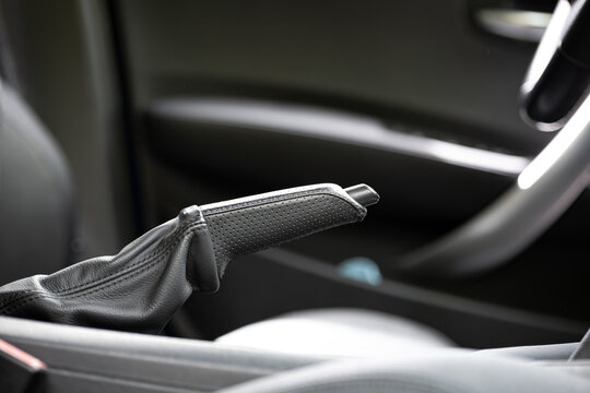 Close up of a black leather manual handbrake lever in a modern car interior with perforated grip texture