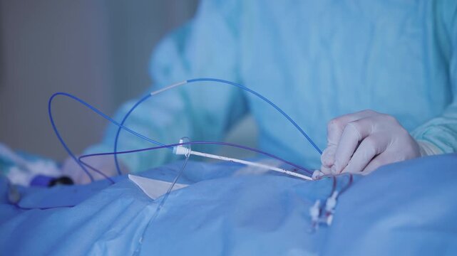 Surgeon hand during cardiac catheter insertion showing hub and sterile gauze on draped chest for clinical procedure.