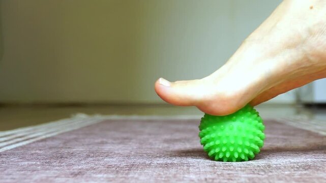 Close-up of slow foot massage using small spiky ball with steady forward and backward movements. Conveys recovery routine, gentle stimulation, and consistent self-care practice at home.