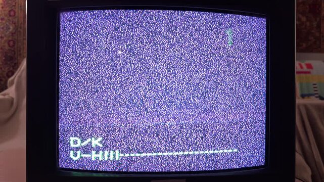 A vintage television screen flickers with purple-tinted static noise and a green number four. This grainy, cold display evokes a lonely or eerie feeling in the dark room.