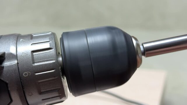 The cordless drill rotates a magnetic bit holder and Phillips head bit at high speed. As the motor spins, it generates a steady, mechanical whirring sound accompanied by a slight metallic vibration.