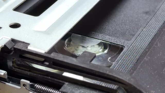 The internal gears and reels of a VCR rotate to play a VHS tape. This action creates a steady mechanical whirring sound combined with rhythmic clicks and the soft hiss of the spinning head.