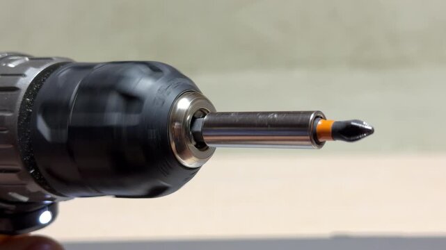 The cordless drill rotates a magnetic bit holder and Phillips head bit at high speed. As the motor spins, it generates a steady, mechanical whirring sound accompanied by a slight metallic vibration.