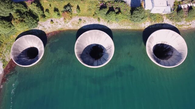Aerial top-down view of three morning glory spillways at Lake Resia dam, Italy. Iconic water infrastructure for hydroelectric power, flood control, and engineering.