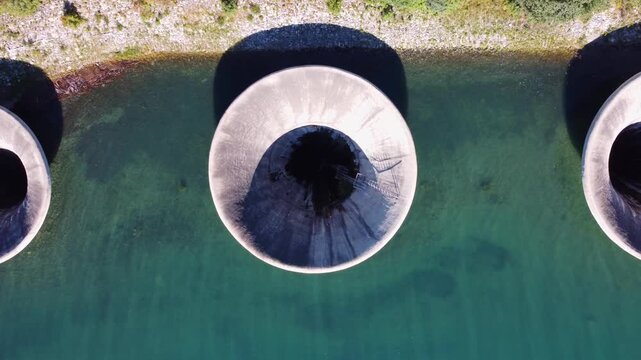 Aerial top-down view of three morning glory spillways at Lake Resia dam, Italy. Iconic water infrastructure for hydroelectric power, flood control, and engineering.