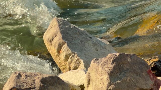 Steady boulders withstand the forceful push of a cold mountain stream. This scene feels grounding and resilient as the energetic water flows by. Bright light sparkles on the moving waves.