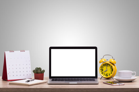Modern workspace setup featuring laptop computer with calendar planner alarm clock and coffee cup on wooden desk