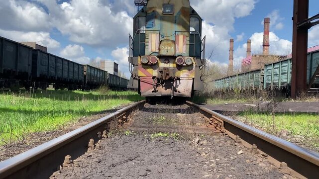 Old diesel locomotive standing on railway tracks at a station against blue sky. Camera moves upward from low angle. Concept of transportation, industry, logistics and rail infrastructure. 4K video.