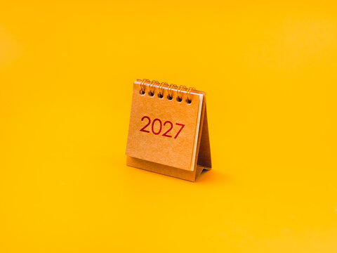 Standing brown paper calendar flip chart displaying the year two thousand twenty seven against bright yellow background