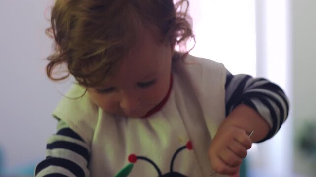 Toddler eating during mealtime as parent feeds with hand then child grabs spoon to eat independently before being fed again with fork, showing learning process and growing autonomy