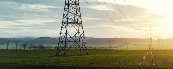 Scenic view of electricity pylons stretching across green fields warm sunset sky background. Electric power supply high voltage metal tower in Europe © Kyryl Gorlov