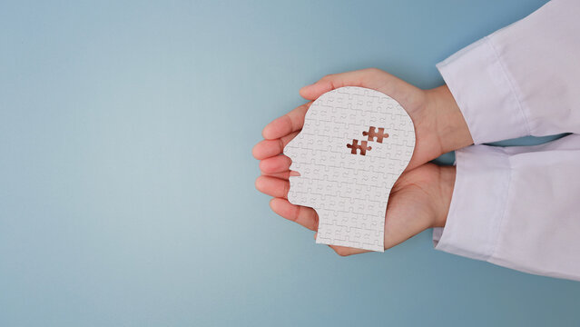 Caring doctor hand holding white paper head with puzzle piece showing visual mental health recovery concept offering gentle support