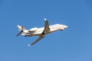 Fototapeta premium Scenic close bottom view modern luxury expensive white private jet plane dispatching from airport isolated on blue clear sky background. Executive aicraft vip travel concept. Service and maintenance