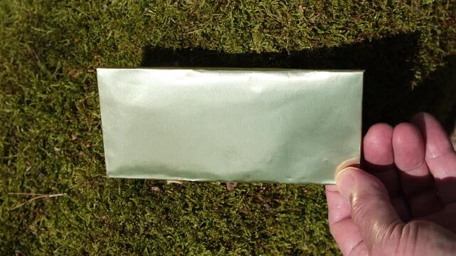 Chocolate bar in paper-based eco-foil with a premium look, in a human hand on a green moss background. Sunlight. Ethical, natural, and organic chocolate. Eco-friendly packaging.