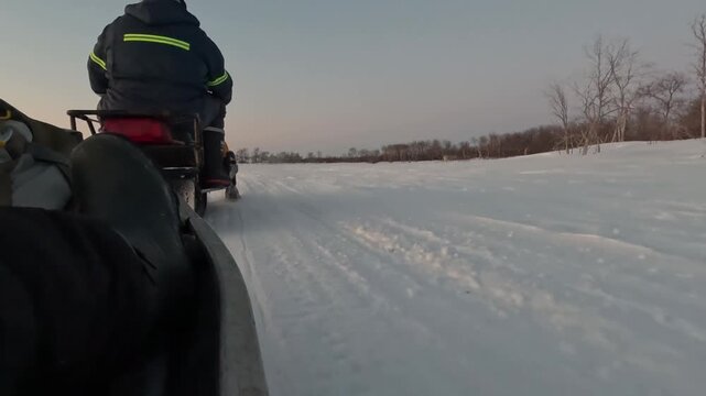 Handheld GoPro shot from the right side of a sled being towed by a snowmobile on frozen Lake Manitoba, Manitoba, Canada. Shoreline with trees visible, driver steering, very cold.