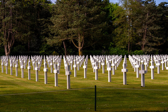 Alignement de croix latines en marbre blanc dans un cimeti&egrave;re militaire verdoyant sous un ciel bleu clair, rendant hommage aux soldats tomb&eacute;s.