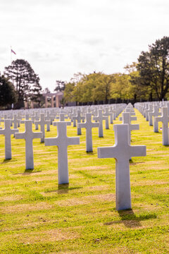 Alignement de croix latines en marbre blanc dans un cimeti&egrave;re militaire verdoyant sous un ciel bleu clair, rendant hommage aux soldats tomb&eacute;s.