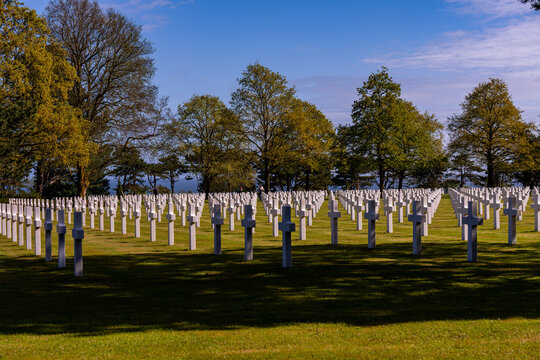 Alignement de croix latines en marbre blanc dans un cimeti&egrave;re militaire verdoyant sous un ciel bleu clair, rendant hommage aux soldats tomb&eacute;s.