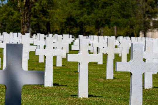 Alignement de croix latines en marbre blanc dans un cimeti&egrave;re militaire verdoyant sous un ciel bleu clair, rendant hommage aux soldats tomb&eacute;s.