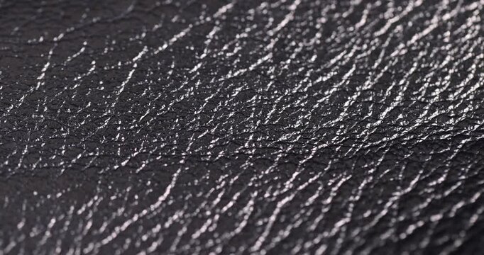 The leather for the bag has deep wrinkles, black genuine leather with a grainy surface and bright highlights in the side light with clear details and organic texture in the macro.