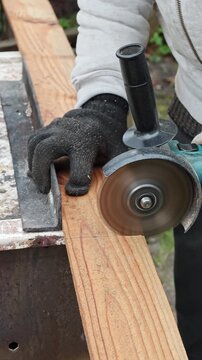A skilled worker, clad in work gloves, meticulously cuts a sturdy wooden board with a powerful angle grinder, generating fine sawdust as they precisely shape the material for a building project or DIY