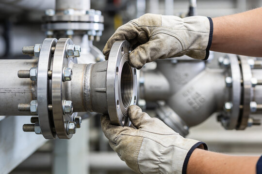 Industrial worker in protective gloves assembling metal pipes with flanges and bolts