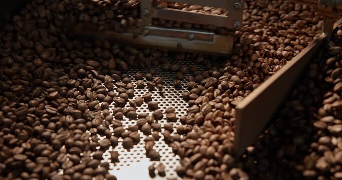 Closeup tracking shot of coffee beans tumbling inside industrial roaster drum with gentle pan motion.