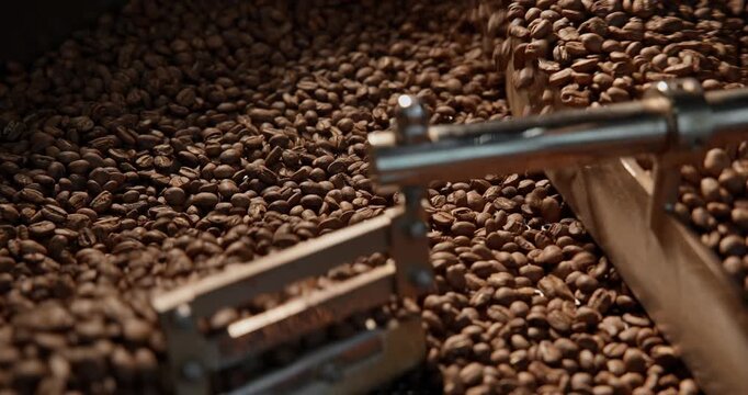 Slow motion coffee beans tumbling and stirring inside industrial roaster production facility.