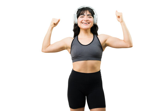 Happy active young woman showing strong arm muscles, feeling powerful and motivated during her workout