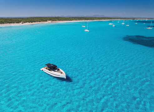 Aerial drone view of a luxury yacht on crystal clear turquoise water near Es Trenc sandy beach, Mallorca, Balearic Islands, Spain. Calm Mediterranean seascape with boats, blue sky and sea. Top view