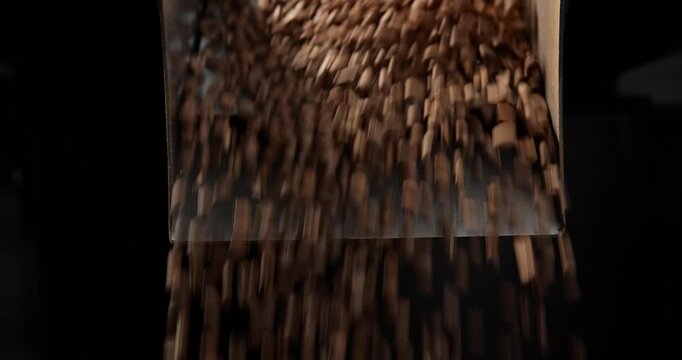 Slow motion coffee beans pouring from industrial roaster drum into industrial hopper, dark light.