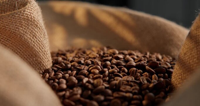 Slow motion close up of fresh aroma roasted coffee beans settling in burlap sack on wooden table in roastery..