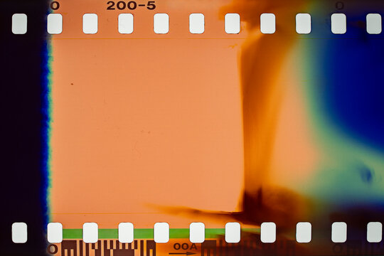 Vintage 35mm film strip scan with orange light leak. Analog film frame with vibrant light leaks, blue chemical stains and sprocket holes. Retro texture for cinematic overlays or nostalgic photography