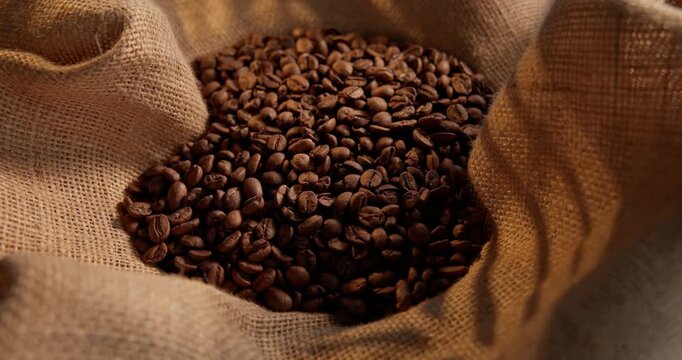 Slow motion closeup of fresh aroma roasted coffee beans in burlap sack on rustic table.
