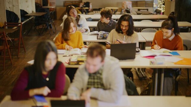 Young students are actively engaged in learning and group work at desks in a modern classroom setting. They are studying, discussing, and utilizing technology for their academic assignments.