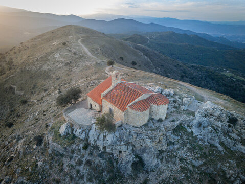 Aerial view of the historic Sant Marti de la Roca chapel perched on a rocky cliff overlooking rolling hills and valleys in Camelas, Occitanie, France.