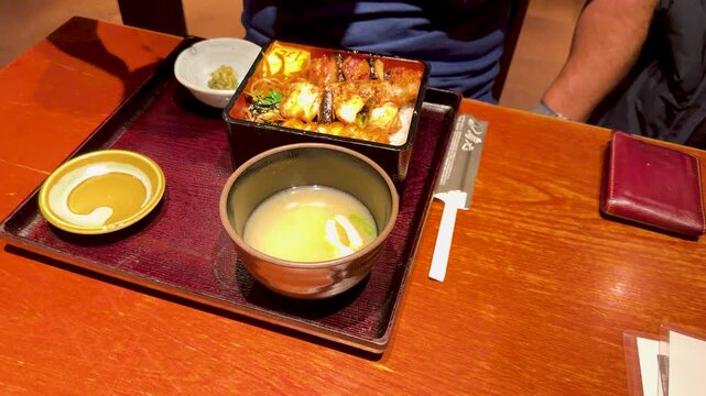 Person stirring hot miso soup with spoon in traditional japanese unagi eel restaurant during lunch time.