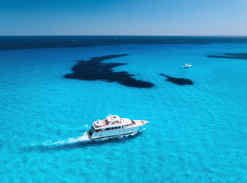 Aerial drone view of luxury yacht moving through shallow turquoise sea above dark rocky seabed, boats anchored nearby, summer scene near Es Trenc, Mallorca, Balearic Islands, Spain. Top view. Seascape
