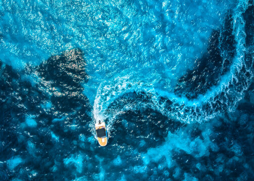 Aerial drone view of small motorboat leaving curved wake in deep blue and turquoise Mediterranean sea, summer scene in Mallorca, Balearic Islands, Spain. Top down view, of speed boat, clear water