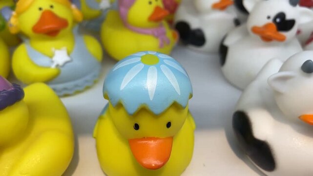 Bright yellow rubber duck toys with painted hats and novelty designs arranged on store display,4K.