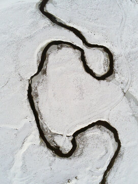 Aerial view of the winding dark river of the Aubrac plateau cutting through a pristine snow-covered landscape Saint-Chely-d'Aubrac, Occitanie, France.