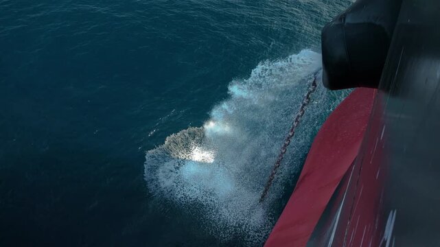 Industrial maritime operation: Anchor lifting with water splashing against the hull.