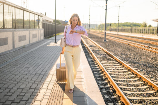 Businesswoman at train station checking the time while walking on the platform, focused on her schedule and travel plans, carrying luggage during a busy commute.