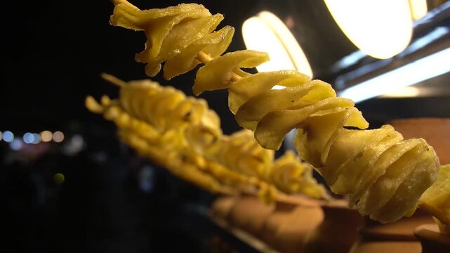 Crispy spiral fries on skewers with warm bokeh background, fast food snack concept