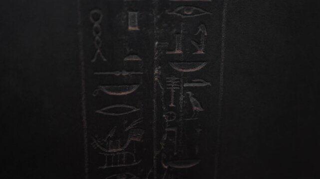 Slow vertical camera movement revealing intricate egyptian hieroglyphs carved on a dark stone surface, concluding on a depiction of a winged goddess, possibly isis or maat