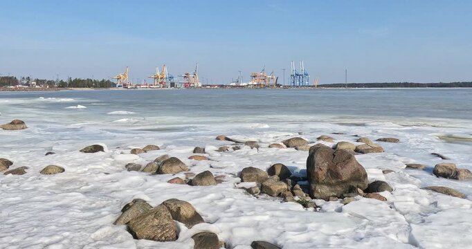 Rocky seashore and frozen sea with view of Vuosaari Harbour in the background in spring, Helsinki, Finland, Europe.