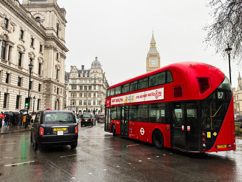 Red double decker bus and black cab on a rainy street near Big Ben in London, UK