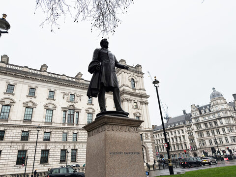 Historic bronze Lord Viscount Palmerston statue on plinth with grand civic buildings in central London, UK